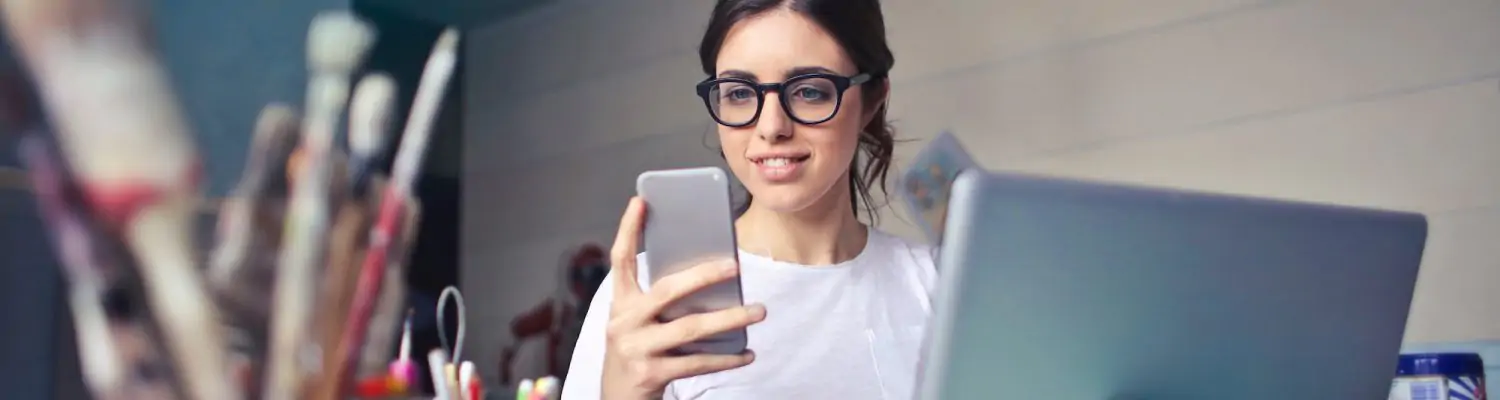 woman in white t shirt holding smartphone in front of laptop 914931